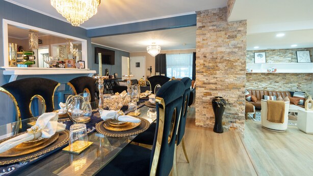Un comedor con una mesa larga dispuesta para una comida, una araña y una pared de piedra.