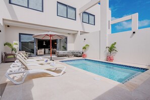 Ein moderner Poolbereich im Freien mit Liegestühlen, einem roten Sonnenschirm und Blumentöpfen.