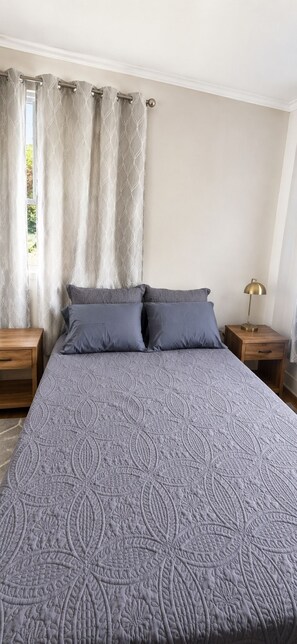 Ein Schlafzimmer mit einem großen Bett, zwei Nachttischen, einer Lampe und Vorhängen.