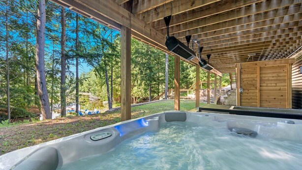 A hot tub under a wooden pergola with a view of a lake and trees. - ✨ Lake Compound | Sauna-Hot Tub-Steam Shower-Cold Plunge (Interlochen)