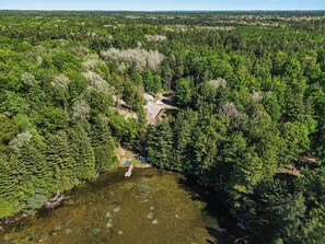 An aerial view of a forested area with a small building surrounded by dense trees and a clear water body.