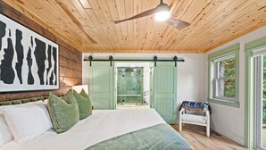 A bedroom with a bed, a green door, a bench, and a window. - ✨ Lake Compound | Sauna-Hot Tub-Steam Shower-Cold Plunge (Interlochen)