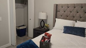 A bedroom with a bed, a nightstand, a lamp, a closet, and a trash bin. - Brand New Luxury Basement (Calgary)