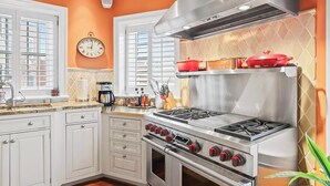 A kitchen with white cabinets, a stainless steel stove, and a clock on the wall. - Sojourn on Swann | Chic 2BD with Rooftop Deck (Washington DC)