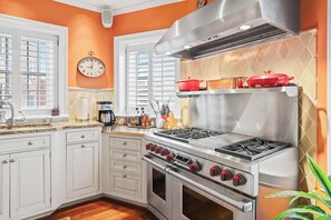 A kitchen with white cabinets, a stainless steel stove, and a clock on the wall. - Sojourn on Swann | Chic 2BD with Rooftop Deck (Washington DC)