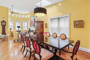 A dining area with a long table, chairs, a chandelier, and a large window. - Sojourn on Swann | Chic 2BD with Rooftop Deck (Washington DC)