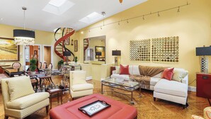 A spacious living room with a staircase, a glass coffee table, and a red ottoman. - Sojourn on Swann | Chic 2BD with Rooftop Deck (Washington DC)