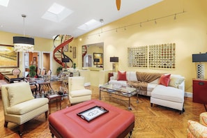 A spacious living room with a staircase, a glass coffee table, and a red ottoman. - Sojourn on Swann | Chic 2BD with Rooftop Deck (Washington DC)