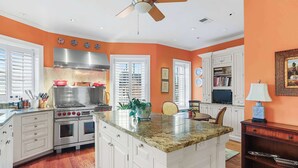 A kitchen with white cabinets, a granite countertop, a stainless steel range hood, and a ceiling fan. - Sojourn on Swann | Chic 2BD with Rooftop Deck (Washington DC)