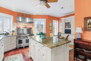 A kitchen with white cabinets, a granite countertop, a stainless steel range hood, and a ceiling fan. - Sojourn on Swann | Chic 2BD with Rooftop Deck (Washington DC)