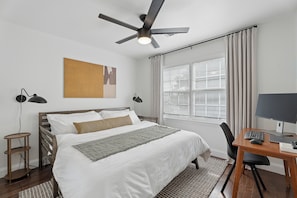 A bedroom with a bed, a desk with a computer, a ceiling fan, and a window with curtains. - Charming Midcentury Modern Beltline Home · 3 Mi to Stadium · Sleeps 6 (Atlanta)