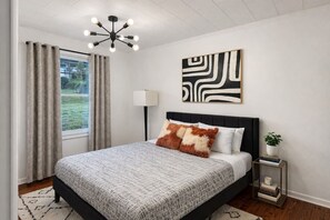 Ein Schlafzimmer mit Bett, Vorhängen, einer Stehlampe, einem Wandbild und einem Nachttisch mit Pflanze.