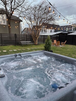 A hot tub with a wooden deck, a tree, and string lights in a backyard setting. - Speakeasy. East Nash. Hot tub. Mins to Broadway (Nashville)