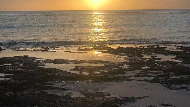 A sunset over a body of water with a rocky shoreline.