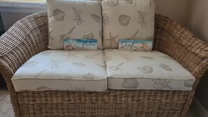 A wicker sofa with two cushions, each featuring a nautical theme with sea creatures and the words 'Relax' and 'Soak' on them.