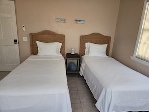 Habitación doble con dos camas individuales, una mesita de noche pequeña con lámpara y un enchufe en la pared.