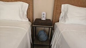 A hotel room with two beds, a bedside table with a lamp, and a small storage space underneath.