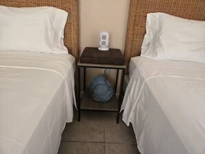 A hotel room with two beds, a bedside table with a lamp, and a small storage space underneath.