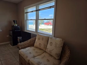 Una habitación con un sofá de mimbre, una cafetera y una ventana que da a un coche rojo y un edificio.