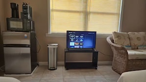 A living room with a TV, a refrigerator, a trash bin, and a wicker sofa.