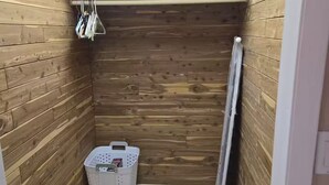 A small, wooden-paneled room with a shelf, a basket, and a radiator.