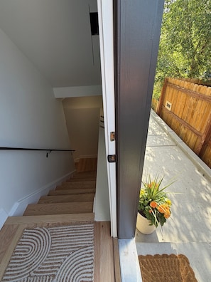 A modern interior with a staircase leading to a second floor, a wooden door, and a potted plant with flowers.