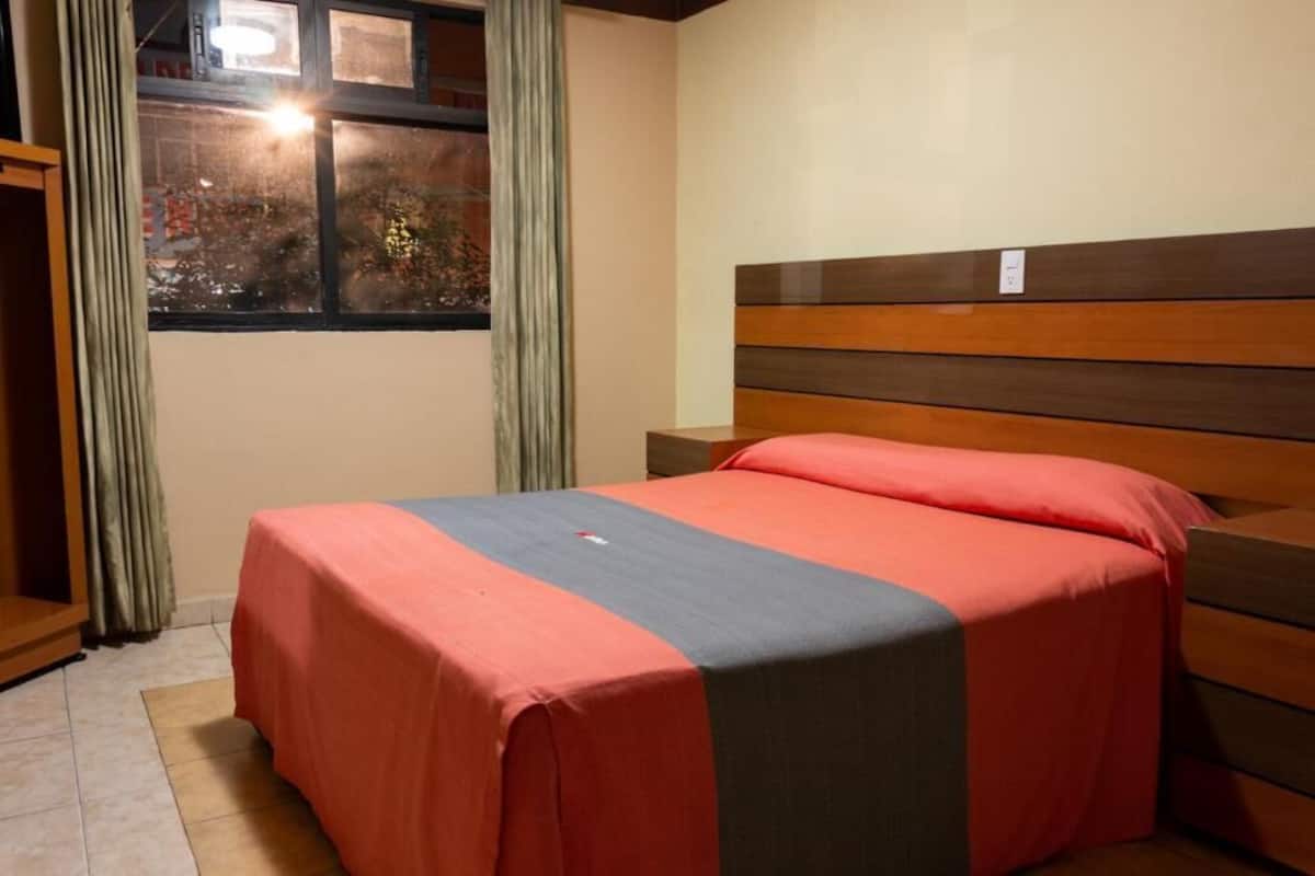 A hotel room with a bed, curtains, a window with a view, and a nightstand.