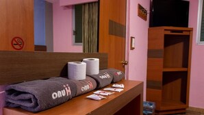 Habitación de hotel con cabecera de madera, un banco con toallas, un cesto de basura y un armario.