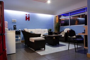 A room with a white sofa, wicker furniture, a coffee machine, and a plant. - Hotel Fabiola (Mexico City)