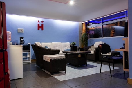 A room with a white sofa, wicker furniture, a coffee machine, and a plant.. Hotel Fabiola