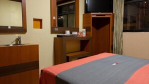 Habitación de hotel con cama, escritorio, espejo, televisor y ventana.