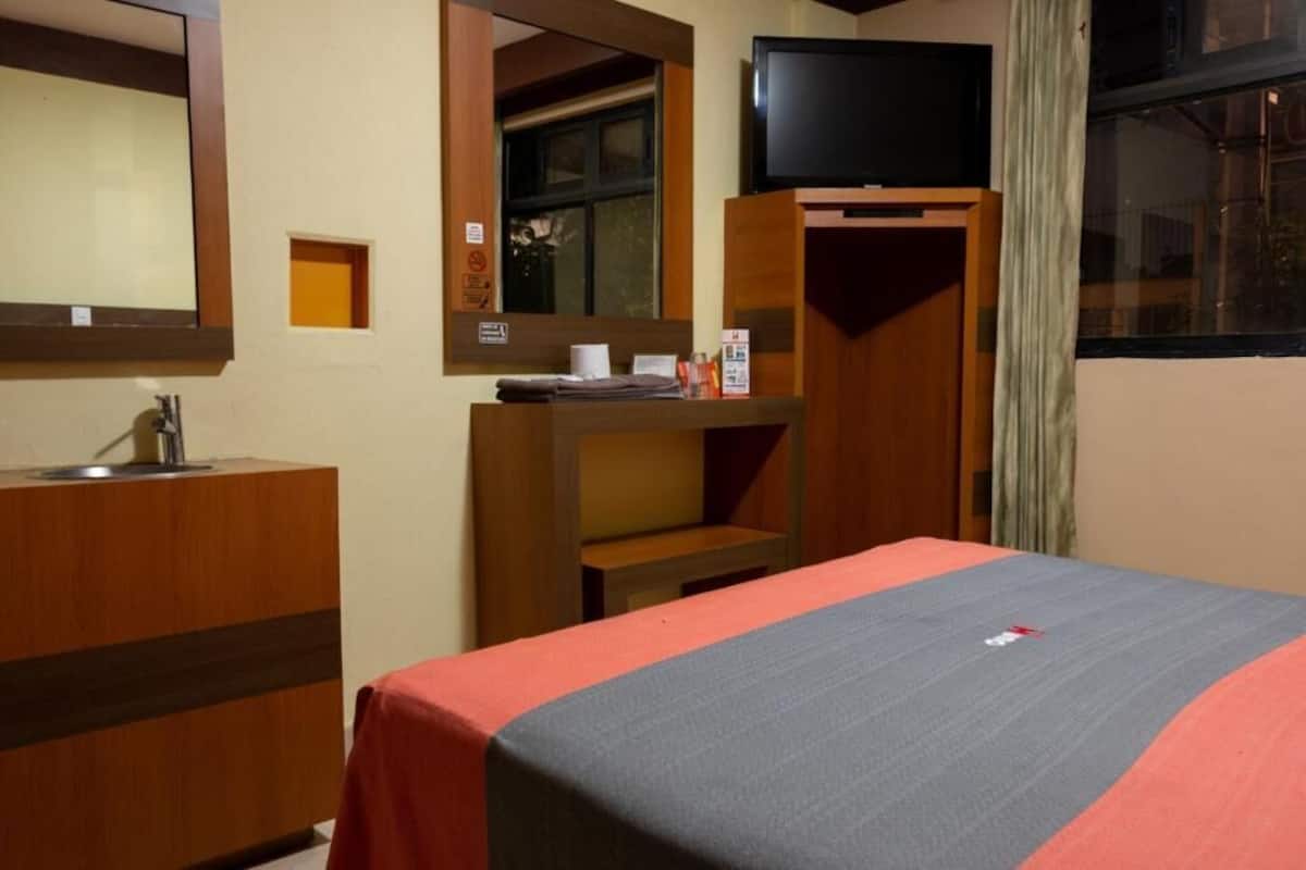 A hotel room with a bed, a desk, a mirror, a television, and a window.
