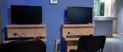 Una habitación con dos monitores, un escritorio, una silla y un estante pequeño con fotos enmarcadas.