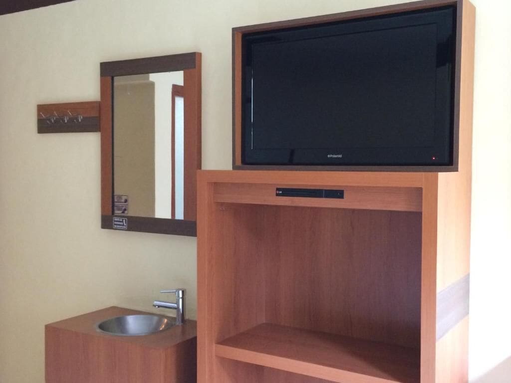 Un baño con tocador de madera, un lavamanos, un espejo y un televisor sobre el tocador.