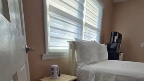 Ein Schlafzimmer mit einem Bett, einem kleinen Tisch mit Kaffeemaschine, einem Fenster mit Jalousien und einer Tür.