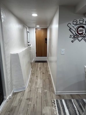 A hallway with a wooden floor, white walls, a door, and a Cubs logo on the wall.