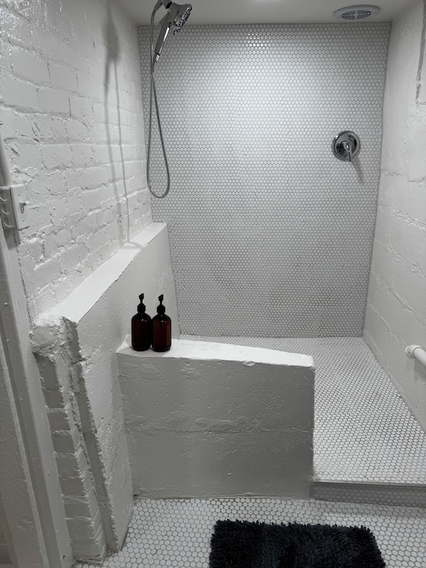 A small, white-walled shower with a textured floor, a handheld showerhead, and two soap dispensers on a ledge.