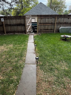 A backyard with a paved path leading to a wooden gate, a shed, and a lawn.