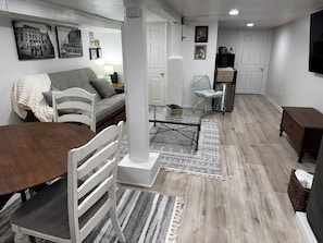 A modern living room with a sofa, dining table, and chairs, a glass coffee table, and a patterned rug.