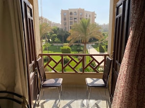 A balcony with two chairs, a decorative railing, and a view of a building and greenery. - Luxury Apartment in Rehab City (Cairo Governorate)
