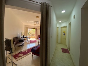 A hotel room with a bed, a desk, a chair, a fan, and a view of the outside. - Luxury Apartment in Rehab City (Cairo Governorate)
