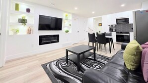 A modern living room with a flat-screen TV, a fireplace, a dining area with chairs, and a kitchen with a microwave. - New 2-Bed Suite in SW Edmonton near Windermere & YEG Airport (Edmonton)