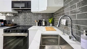 A modern kitchen with a microwave, oven, sink, and a backsplash of dark tiles. - New 2-Bed Suite in SW Edmonton near Windermere & YEG Airport (Edmonton)