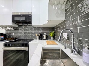 A modern kitchen with a microwave, oven, sink, and a backsplash of dark tiles. - New 2-Bed Suite in SW Edmonton near Windermere & YEG Airport (Edmonton)