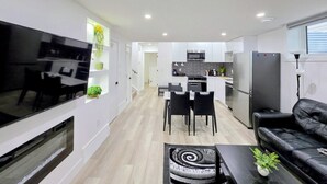 A modern living room with a flat-screen TV, a fireplace, a dining area with a table and chairs, and a kitchen with a refrigerator and microwave. - New 2-Bed Suite in SW Edmonton near Windermere & YEG Airport (Edmonton)