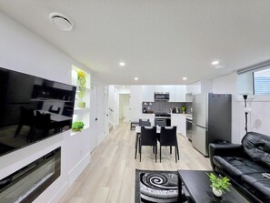 A modern living room with a flat-screen TV, a fireplace, a dining area with a table and chairs, and a kitchen with a refrigerator and microwave. - New 2-Bed Suite in SW Edmonton near Windermere & YEG Airport (Edmonton)