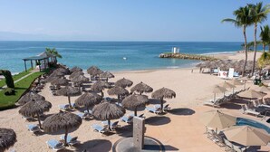 Un resort en la playa con sombrillas de paja, sillas de descanso y una zona de piscina.