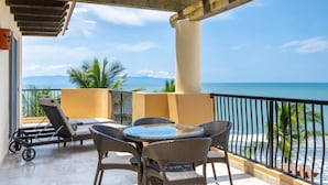 Un balcón con mobiliario de mimbre, una mesa de vidrio y vista al mar.