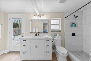 A bathroom with a white vanity, a large mirror, a toilet, a shower with a glass door, and a small window. - 4BR Heated Pool Near Beach | Good Morning Rentals (Jacksonville Beach)