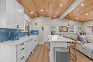 A modern kitchen with white cabinets, a blue coffee maker, and a wooden ceiling. - 4BR Heated Pool Near Beach | Good Morning Rentals (Jacksonville Beach)